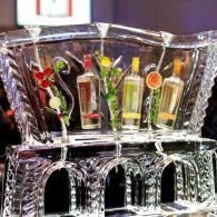 Ice sculpture bar holding colorful cocktail glasses and garnishes at an event
