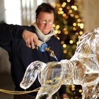 Artist pouring molten glass over a transparent horse sculpture in a workshop