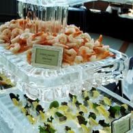 Tiered seafood display with shrimp and lemon wedges on a clear glass tray