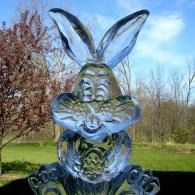 Transparent rabbit ice sculpture on grass with trees and blue sky in the background