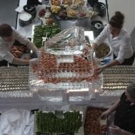People arranging food around a pyramid-shaped ice sculpture on a buffet table