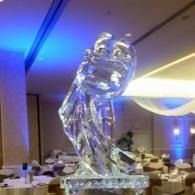 Clear ice sculpture on a banquet table in a dimly lit event hall with blue lighting