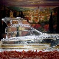 Clear glass ship-shaped sculpture on red pebbles, with a colorful landscape painting in the background