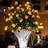 Orange roses in a tall white vase at a dimly lit event