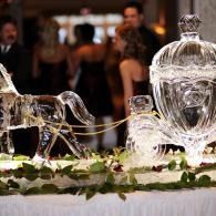 Ice sculpture centerpiece of a horse drawn Cinderella coach at a formal event with guests blurred in the background