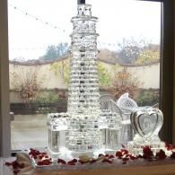 Clear glass tower centerpiece on a windowsill, surrounded by red flower petals, with a frosted heart decoration nearby