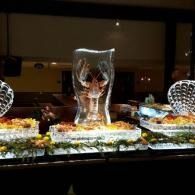Illuminated ice sculpture on a buffet table with floral arrangements in a dim banquet hall