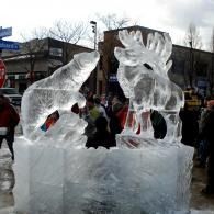 Clear ice sculpture of a wolf and moose in a snowy outdoor crowd scene