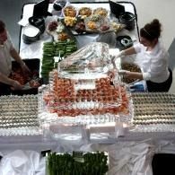 Buffet table with trays of food and fruit, seen from above, with two people serving at the sides