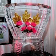 Clear crystal vase with pink flowers and gold leaf accents on a dark surface