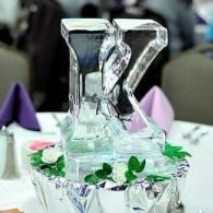 Ice sculpture of the letter K on a decorated table with flowers and purple napkins