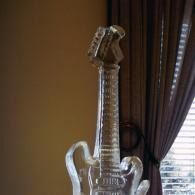 Glass guitar sculpture on a table beside a window with dark curtains