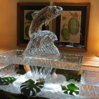 Ice fountain with a sculpted fish centerpiece and green leaves in a warmly lit room