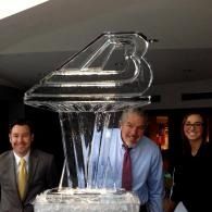 Large glass ice sculpture with three people standing behind it in an indoor event setting