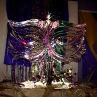 Colorful metallic butterfly wings display with purple and green accents on a stage backdrop