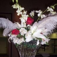 Floral arrangement with white lilies, red roses, and white feathers in a glass vase