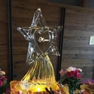 Crystal star-and-dress sculpture with a glowing heart centerpiece, surrounded by flowers indoors