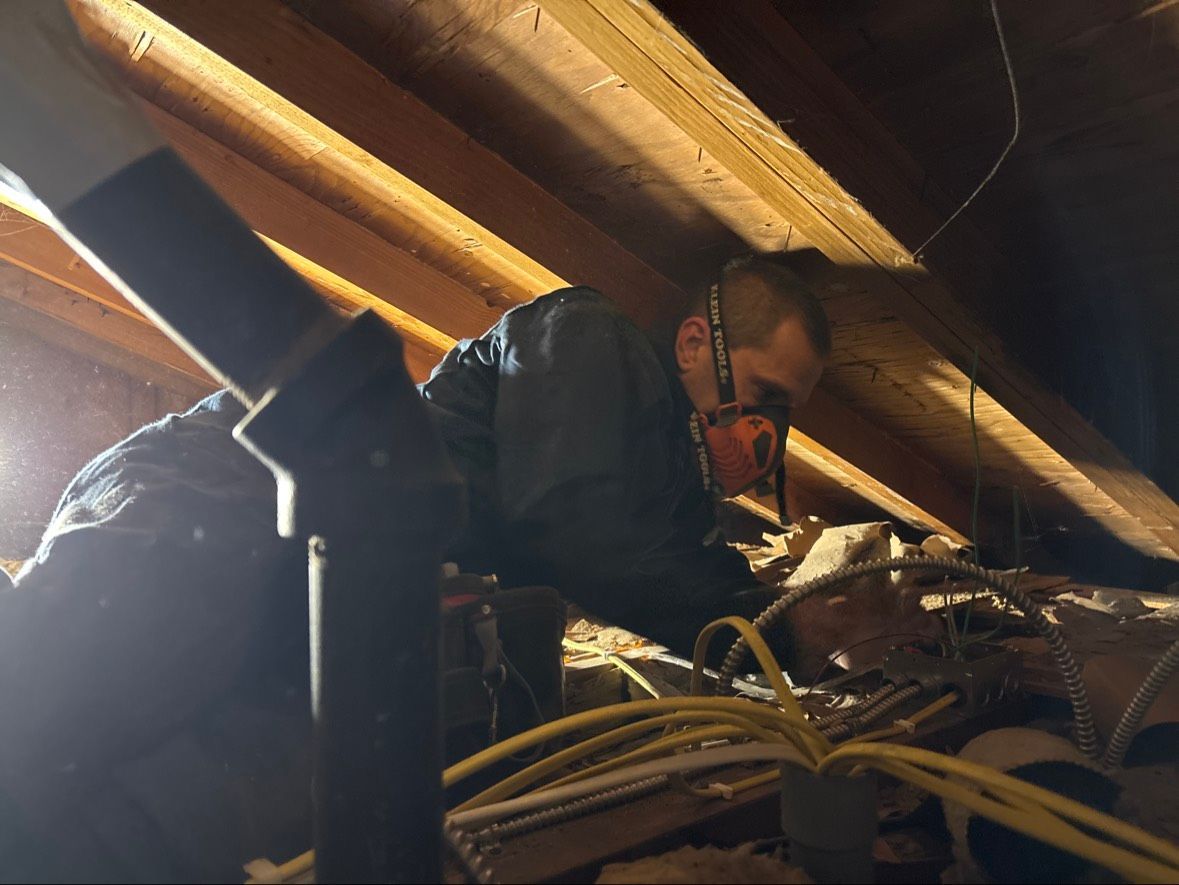 Person working among wooden beams and tangled wires in a dim attic space