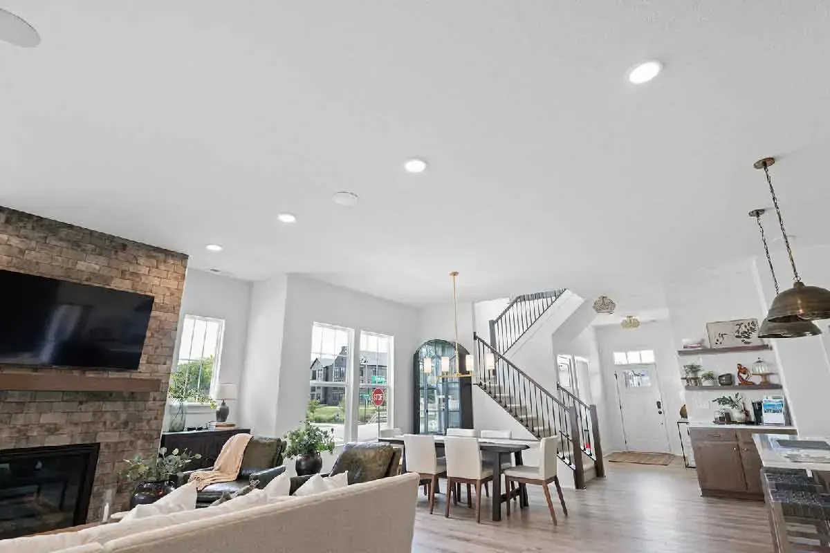 A bright open-concept living room with a stone fireplace, staircase, dining area, and neutral decor.