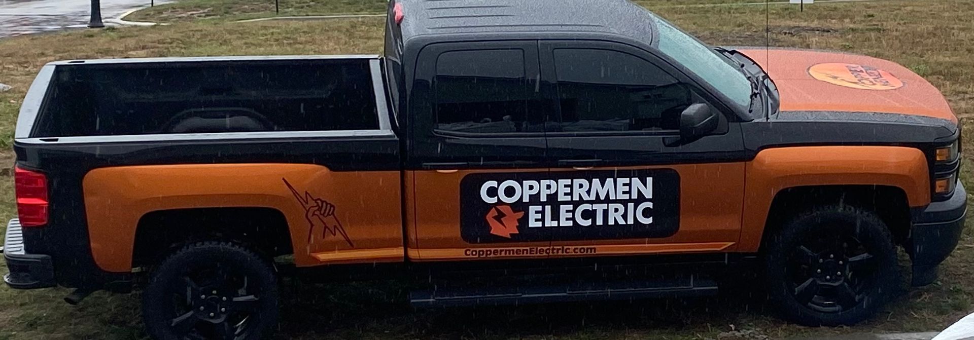 Orange-and-black COPPERMEN ELECTRIC pickup truck parked on grass, side view
