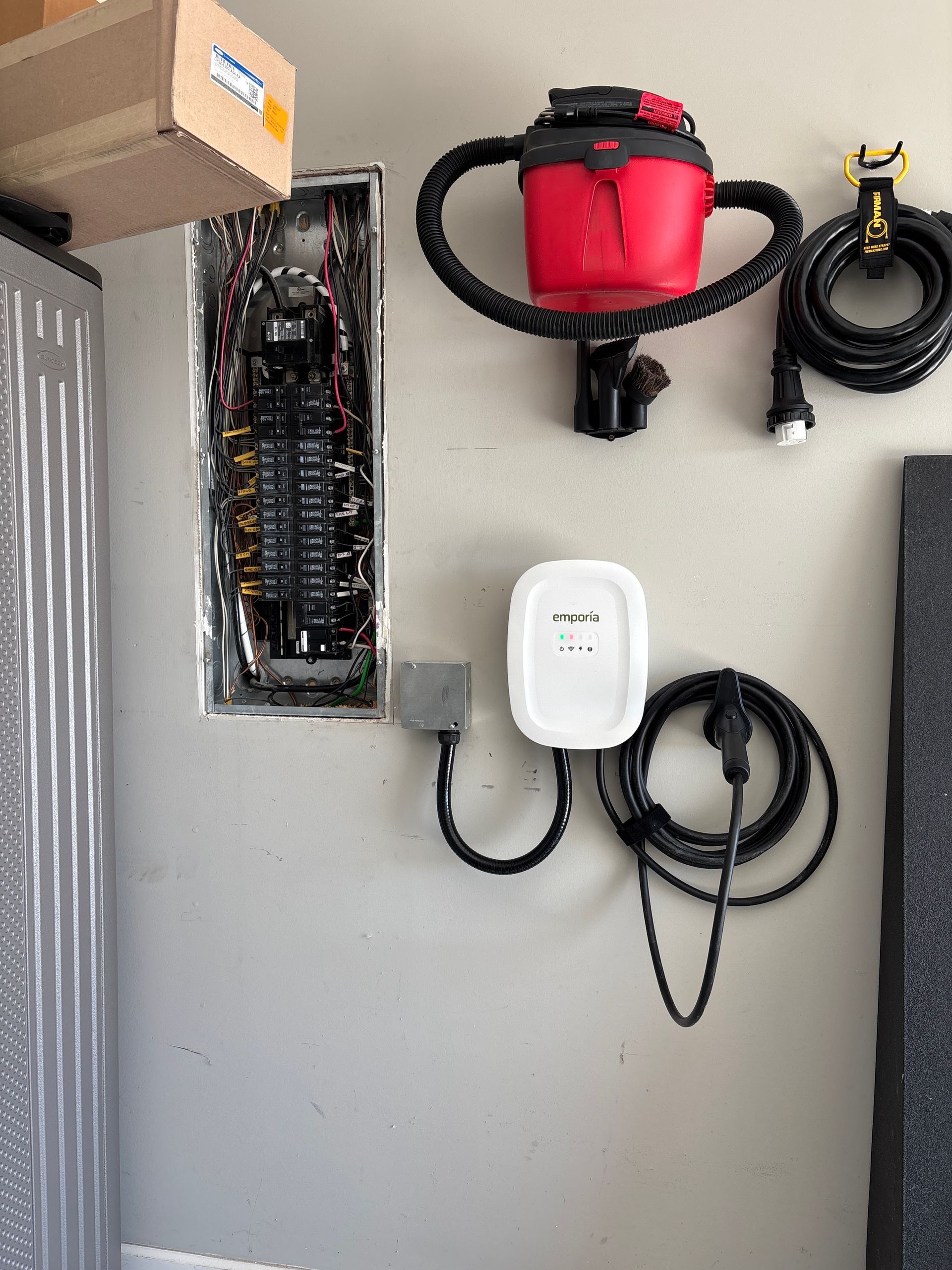 Wall-mounted electrical equipment and coiled cables on a gray surface, including a red canister and white device.