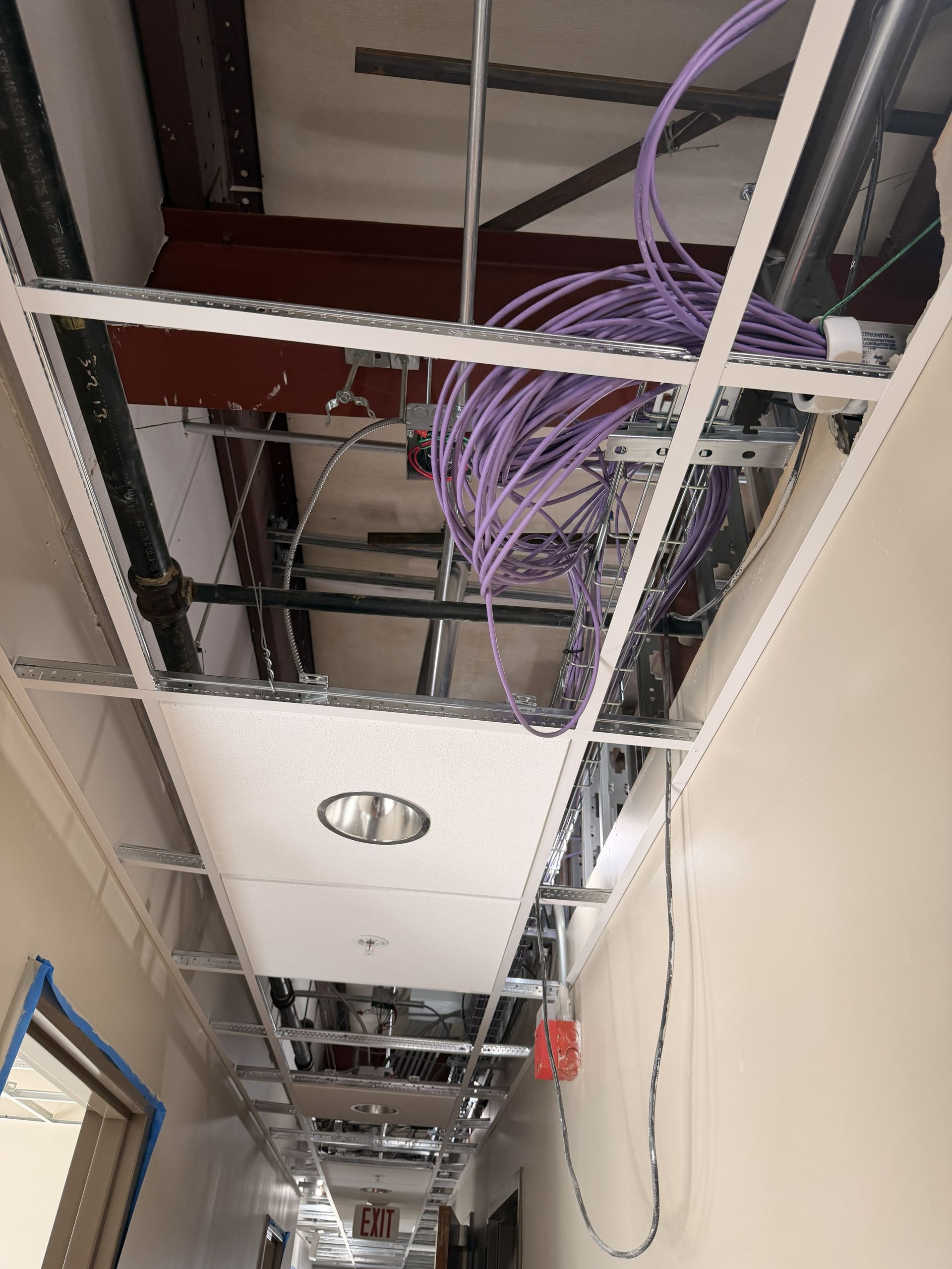 Ceiling under construction with exposed wiring, metal framing, and hanging purple cables in a hallway