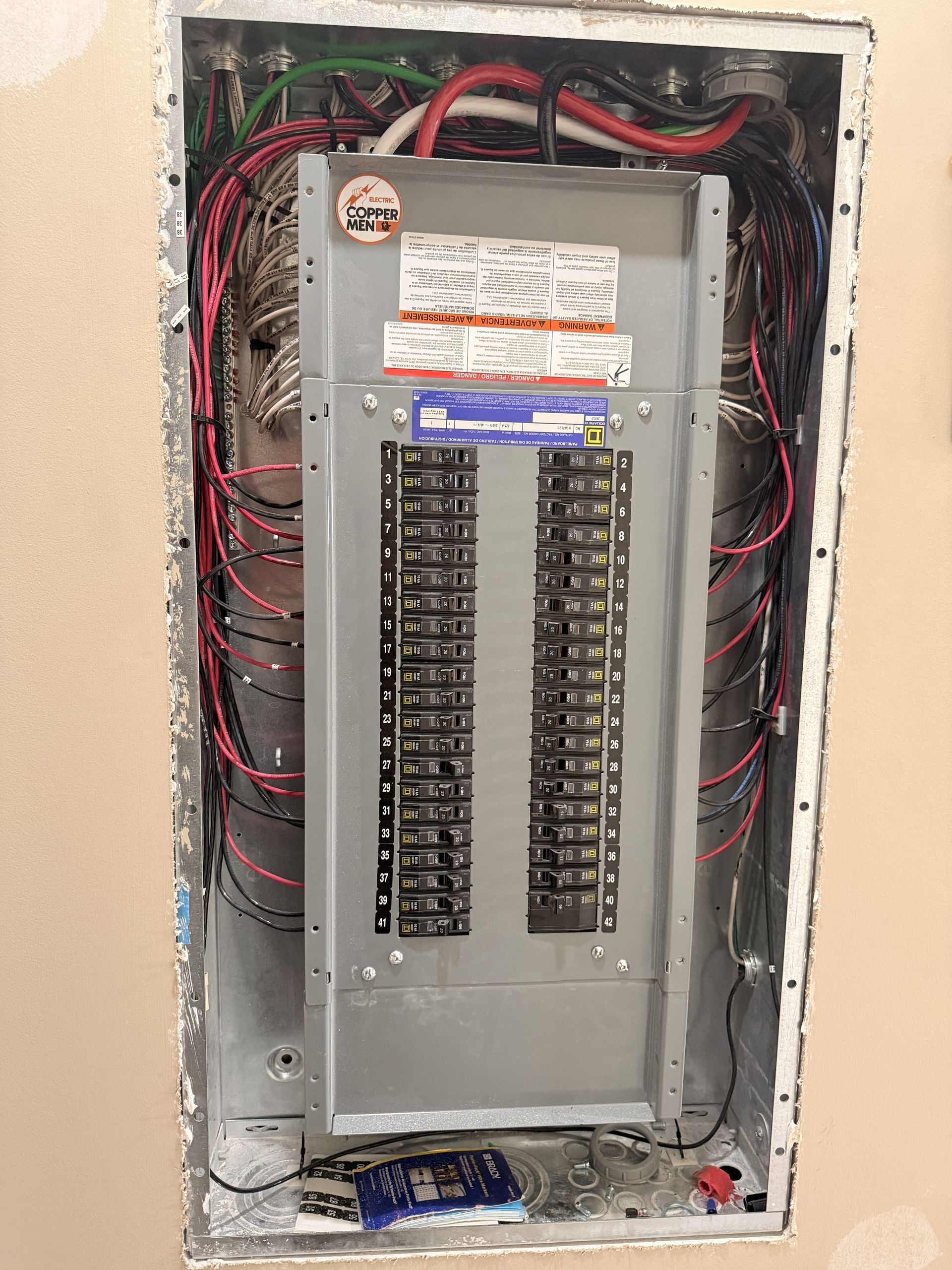 Open electrical breaker panel with exposed wiring and missing cover in a wall opening.