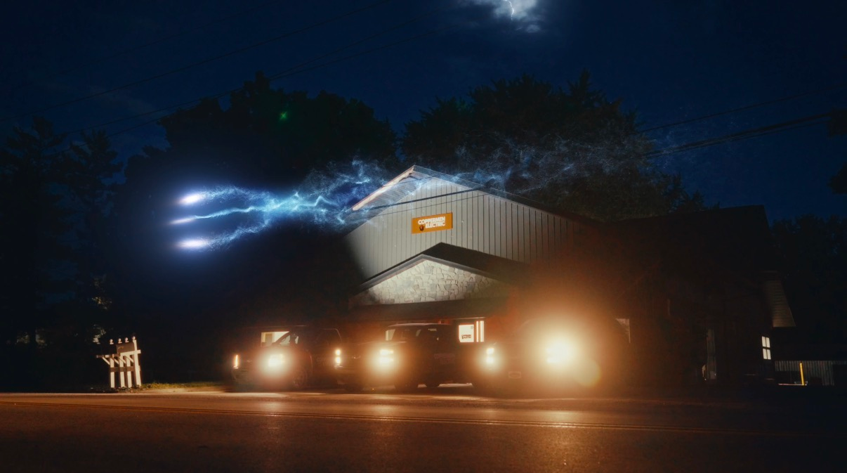 Nighttime industrial building with bright headlights and blue electric arcs in the sky