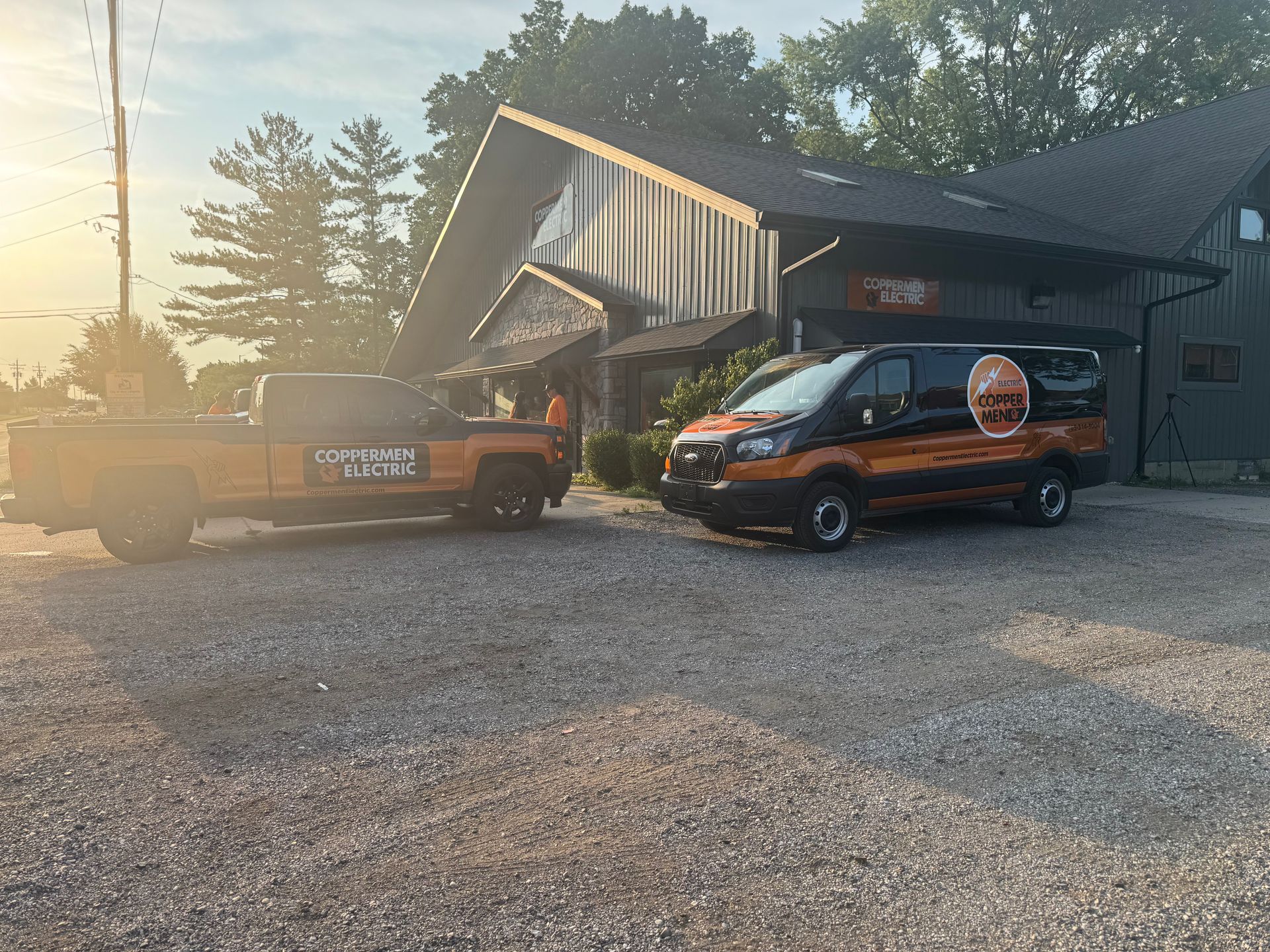Two vintage cars parked on gravel outside a cabin at sunset