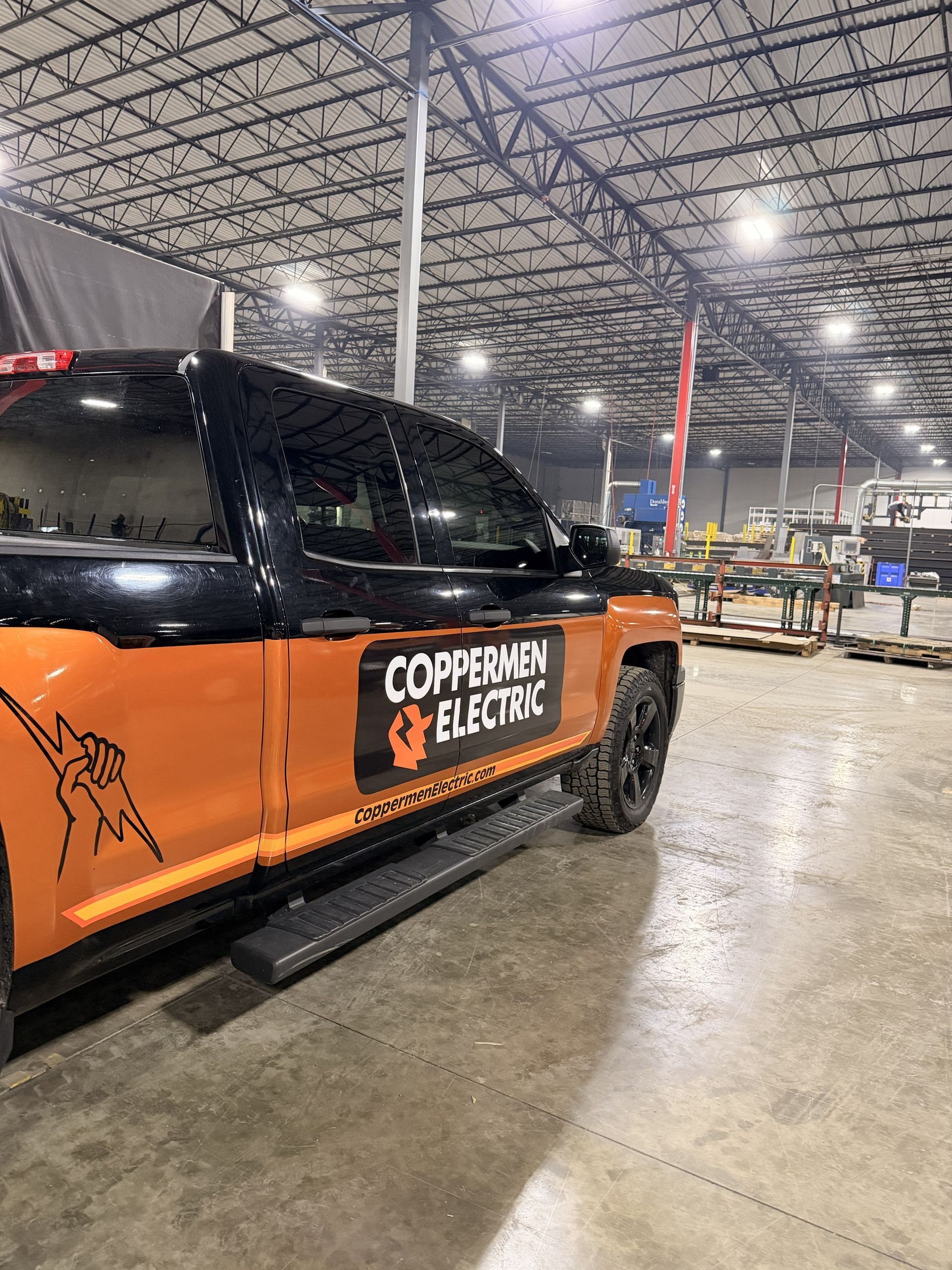 Orange-and-black pickup truck with “Copperview Electric” branding in a warehouse aisle