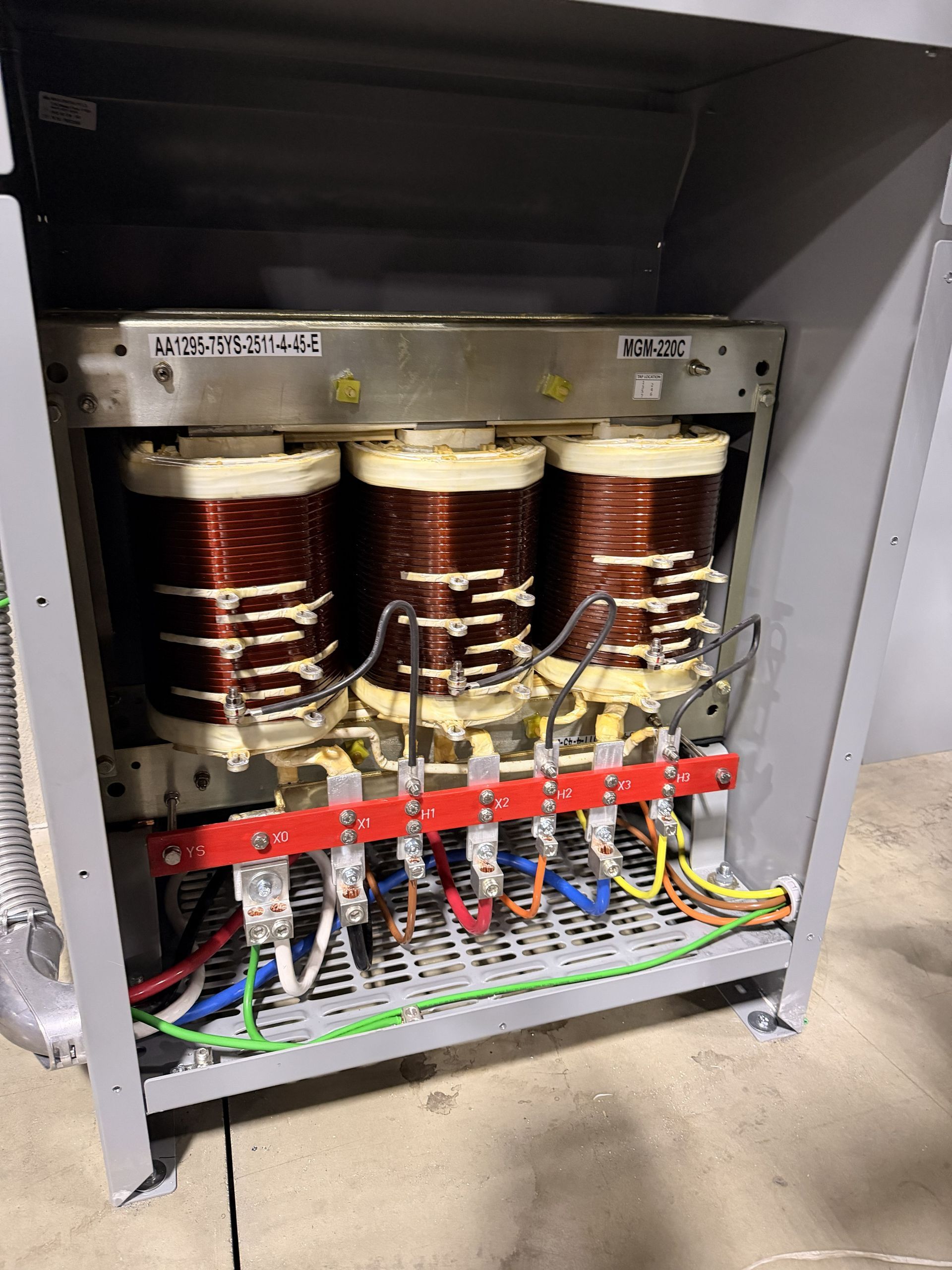 Open electrical cabinet with three copper wire coils, red terminal strip, and colored wiring inside.