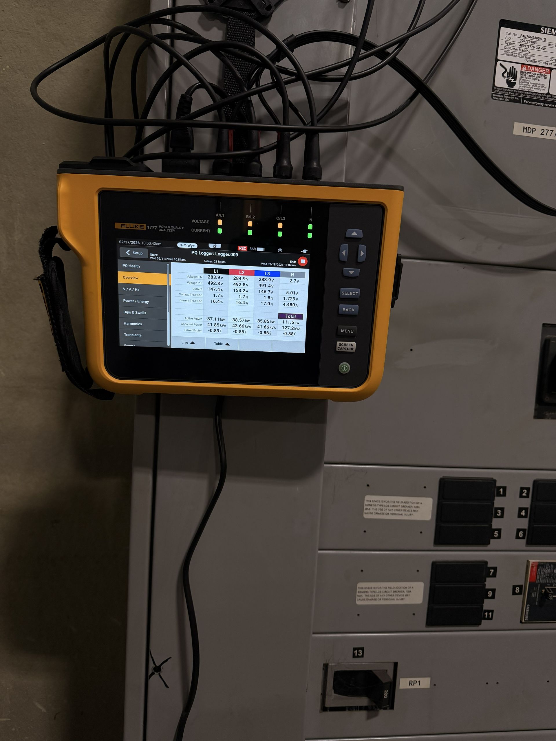 Yellow handheld control display mounted beside electrical panels with cables above it.