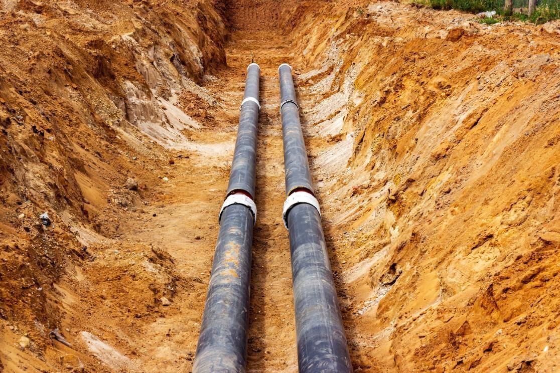 Two black pipes running through a dirt trench with orange soil walls