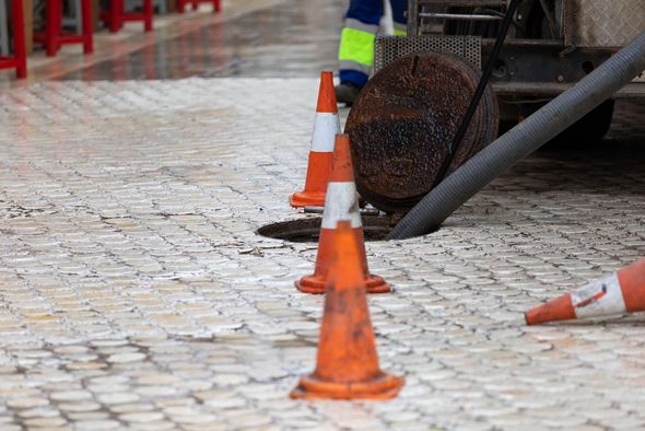 Orange traffic cones on a wet cobblestone street near a sewer