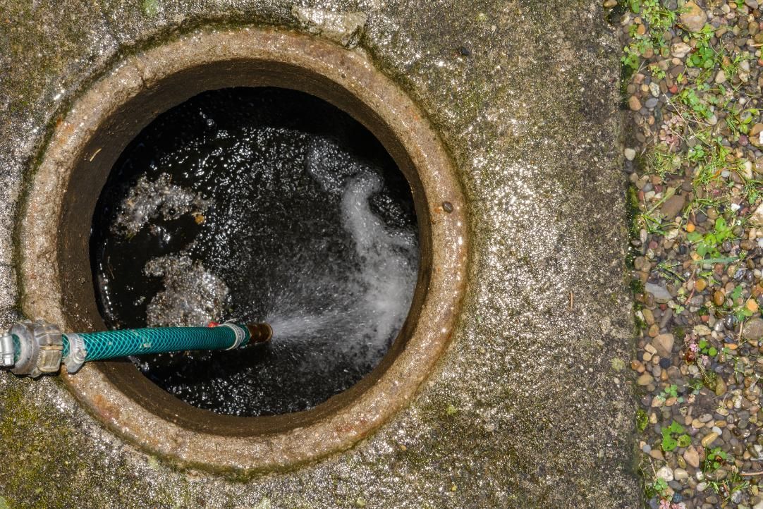 Open drain with rushing water and a hose on a concrete surface