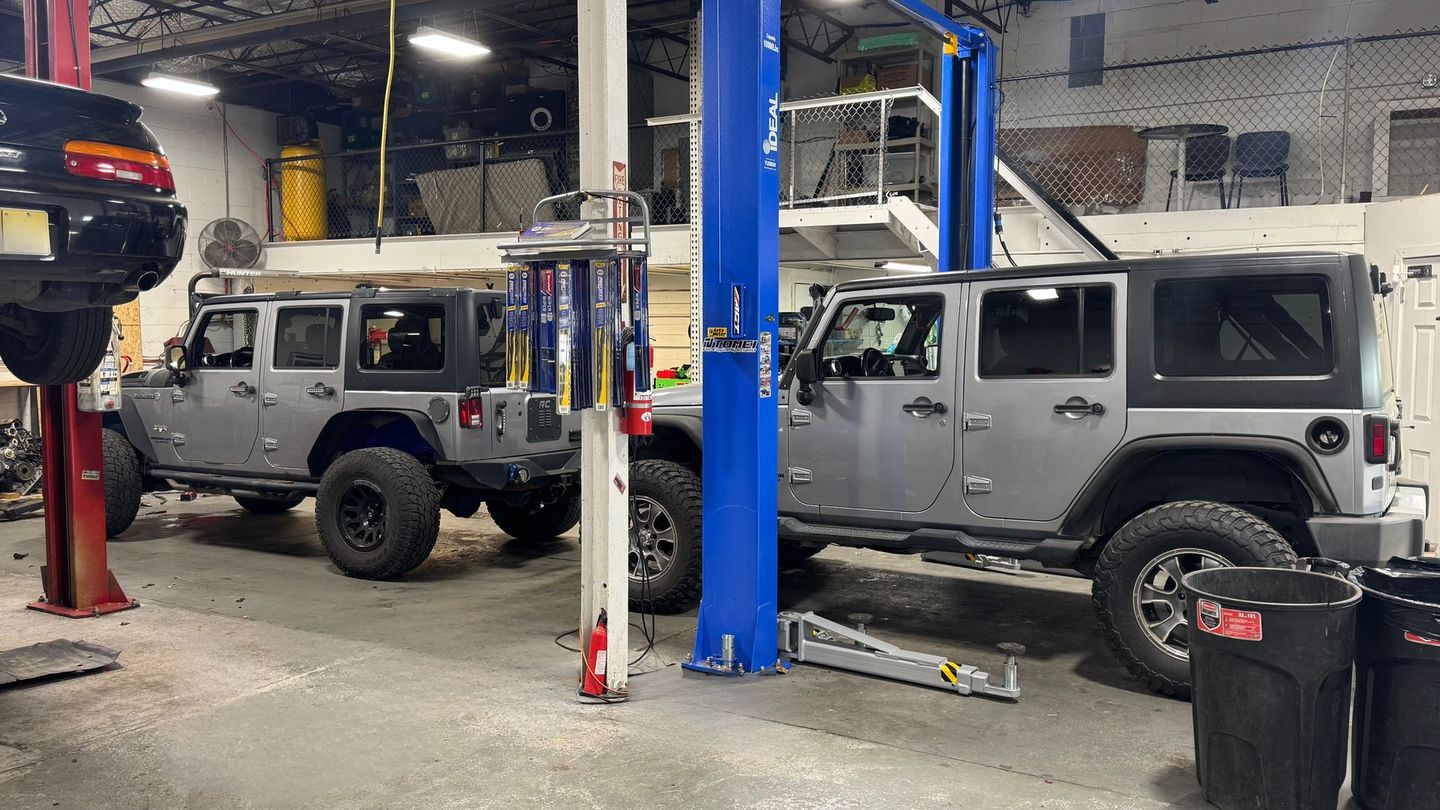 Two silver Jeep Wranglers inside a garage, next to a lift, and equipment. | CT Auto LLC