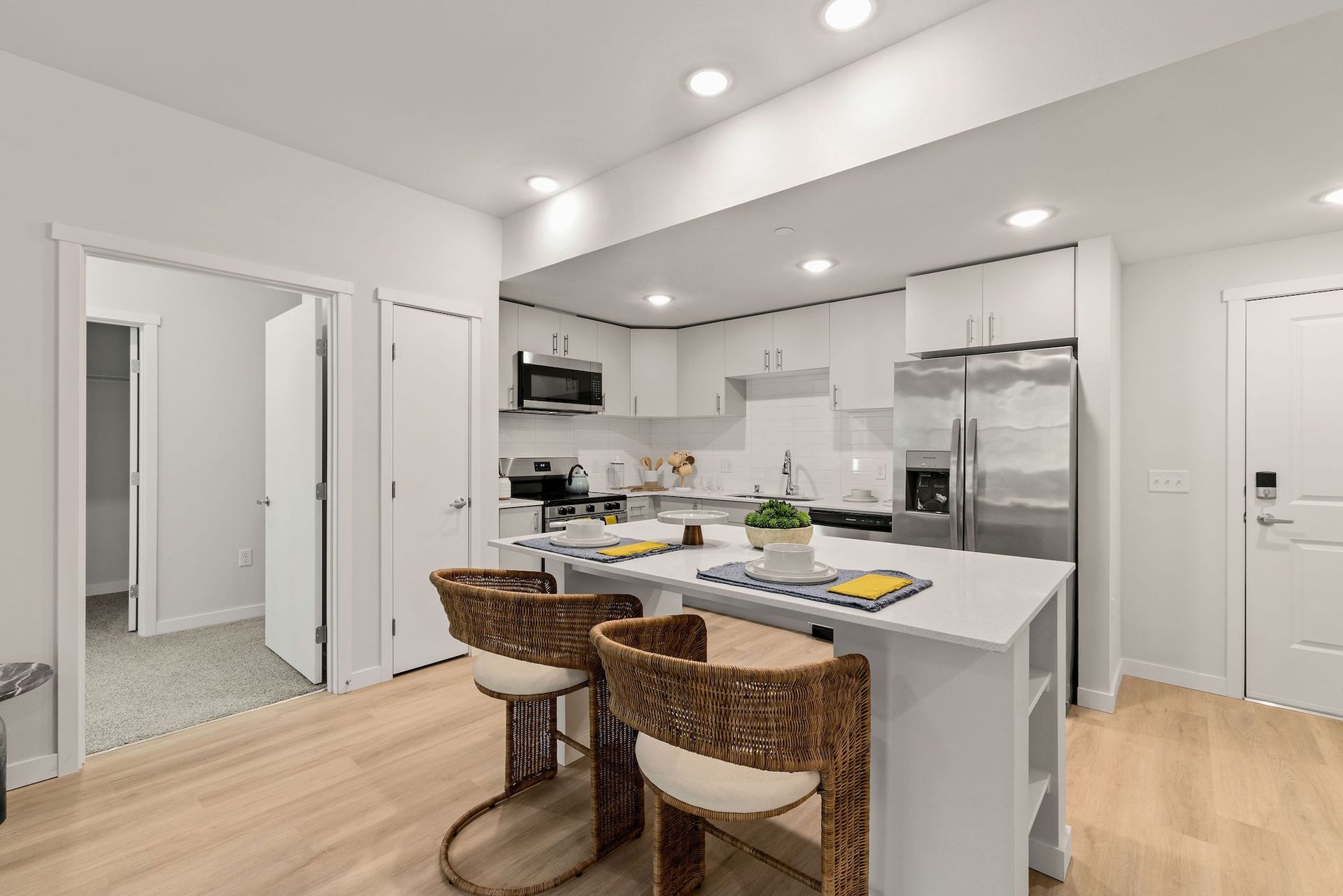 Bright modern kitchen with white cabinets, stainless appliances, and two wicker bar stools at the island