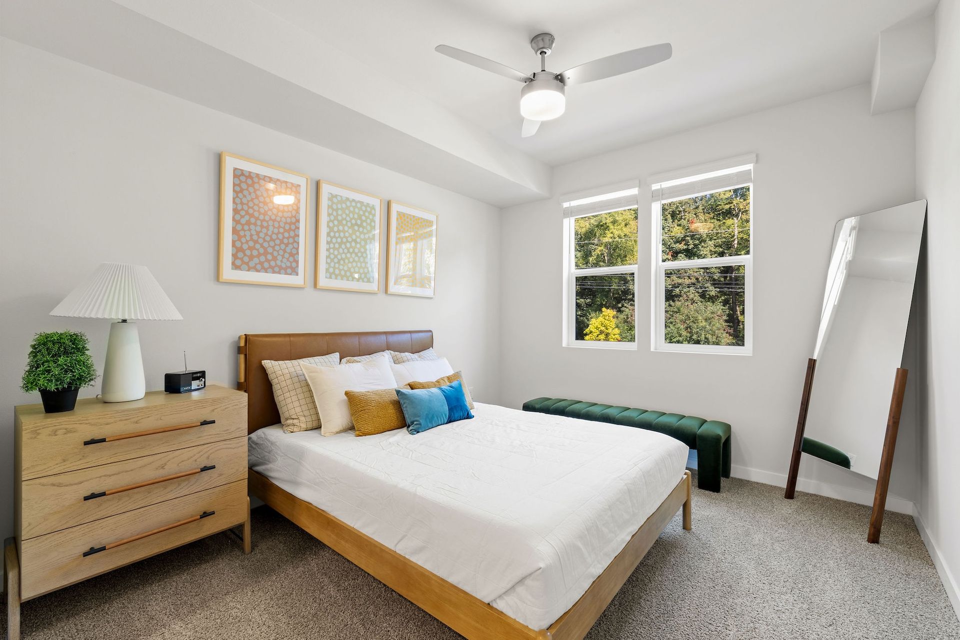 Bright bedroom with a wooden bed, dresser, mirror, and large windows in daylight