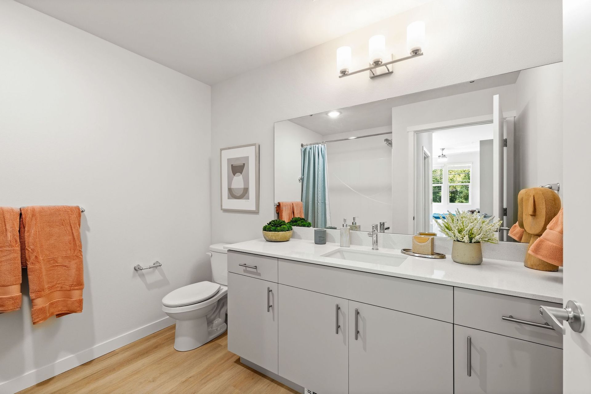 Bright bathroom with double vanity, white walls, orange towels, and a shower visible in the mirror.