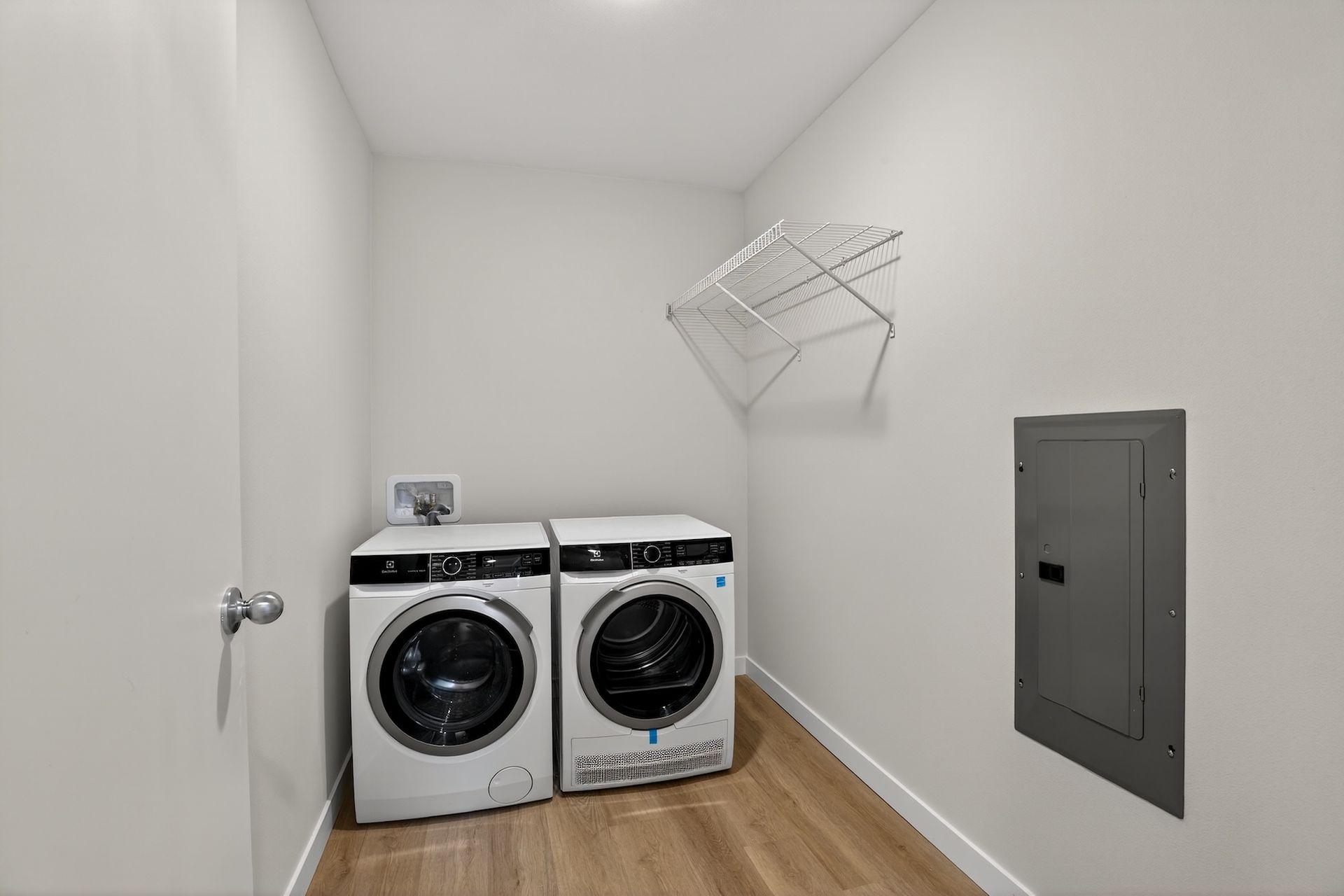Laundry room with side-by-side washer and dryer, wall-mounted drying rack, and utility panel.