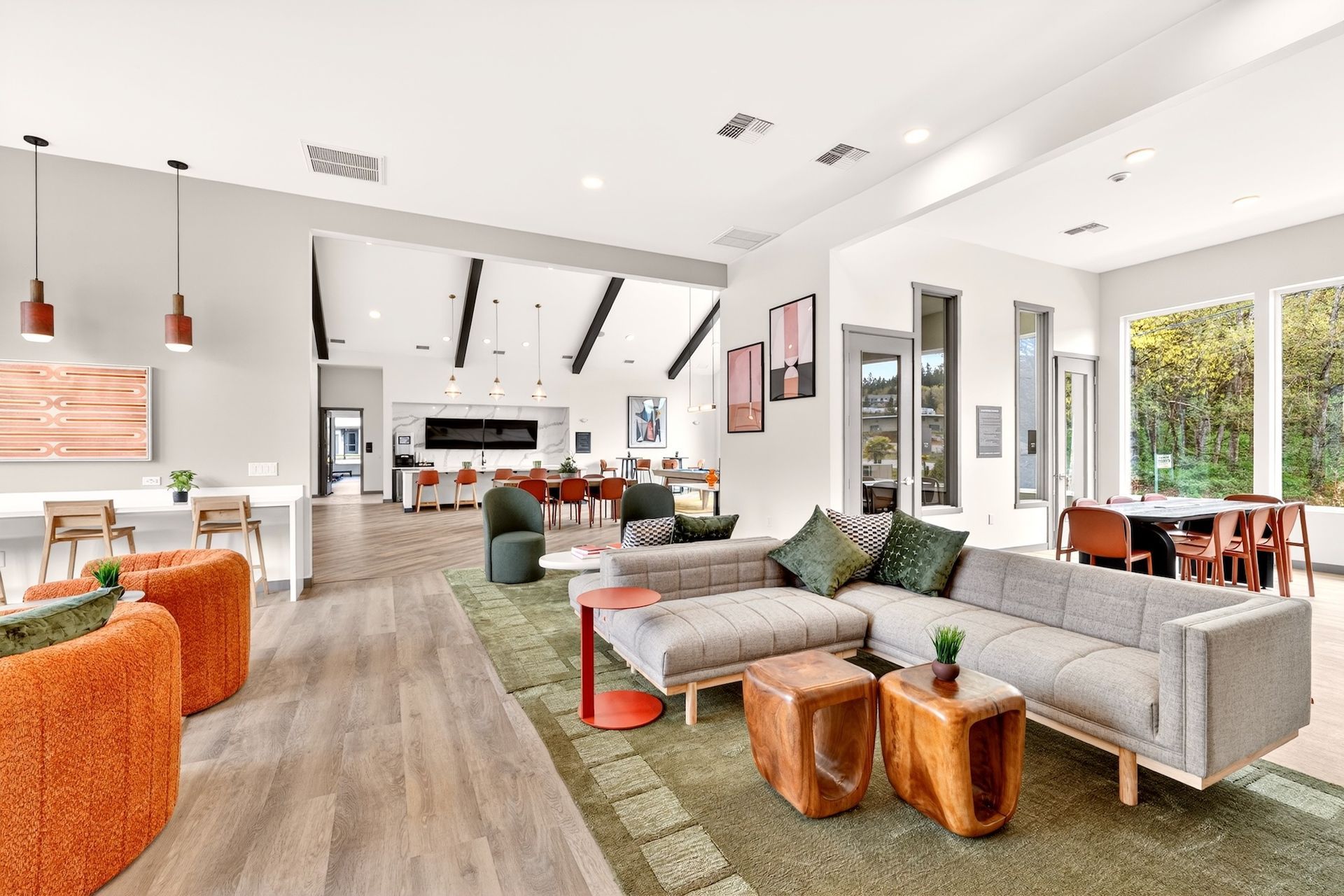 Bright open-plan living room with gray sectional, orange chair, wood floor, and kitchen in background