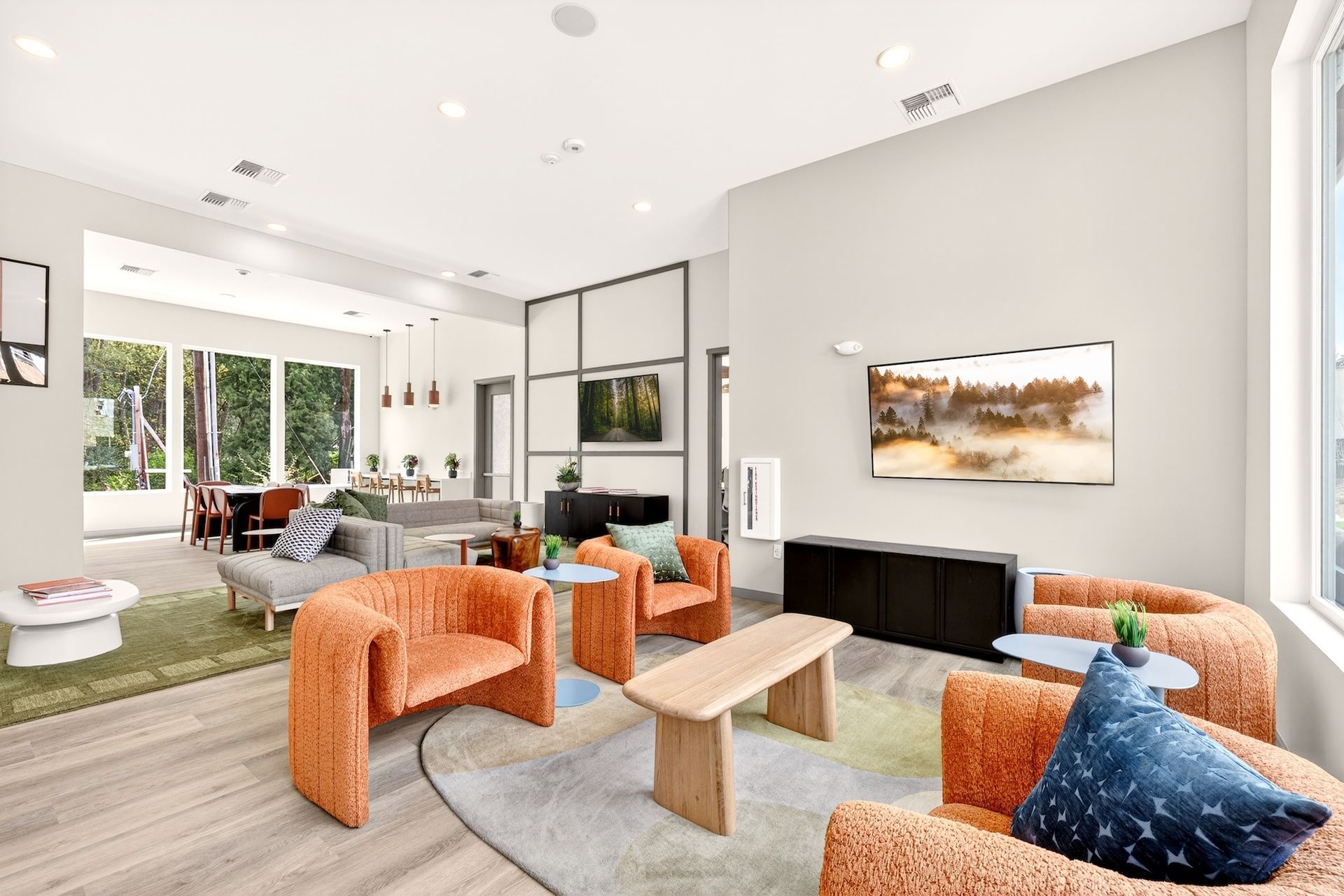Bright modern living room with orange chairs, gray sofa, fireplace, and open dining area with garden view