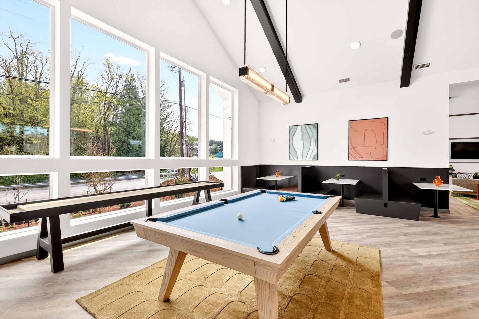 Modern game room with a pool table, benches, large windows, and black ceiling beams