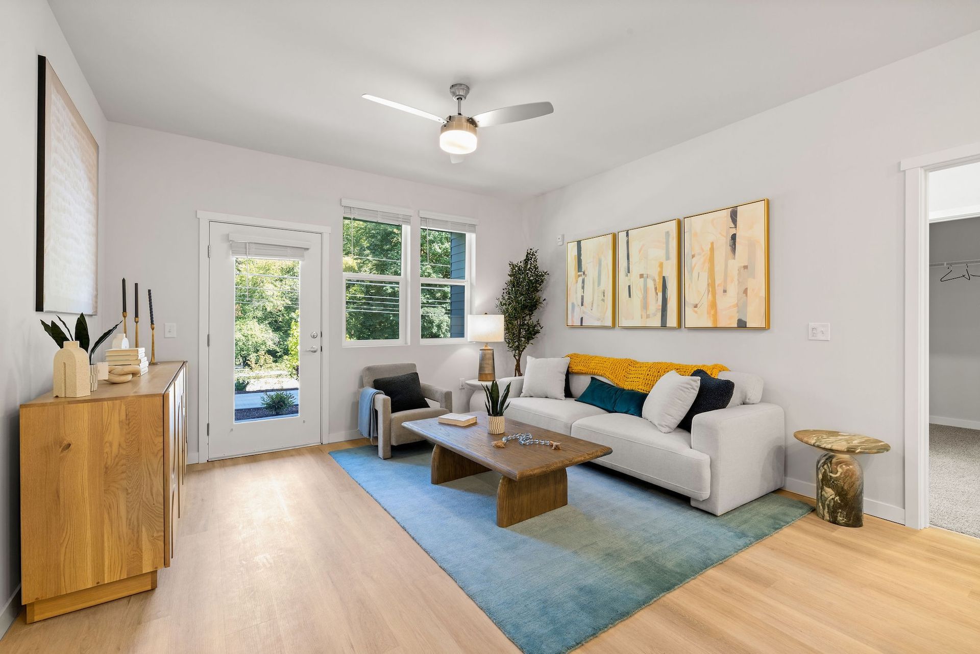 Bright modern living room with gray sofa, blue rug, wooden table, and patio doors overlooking greenery