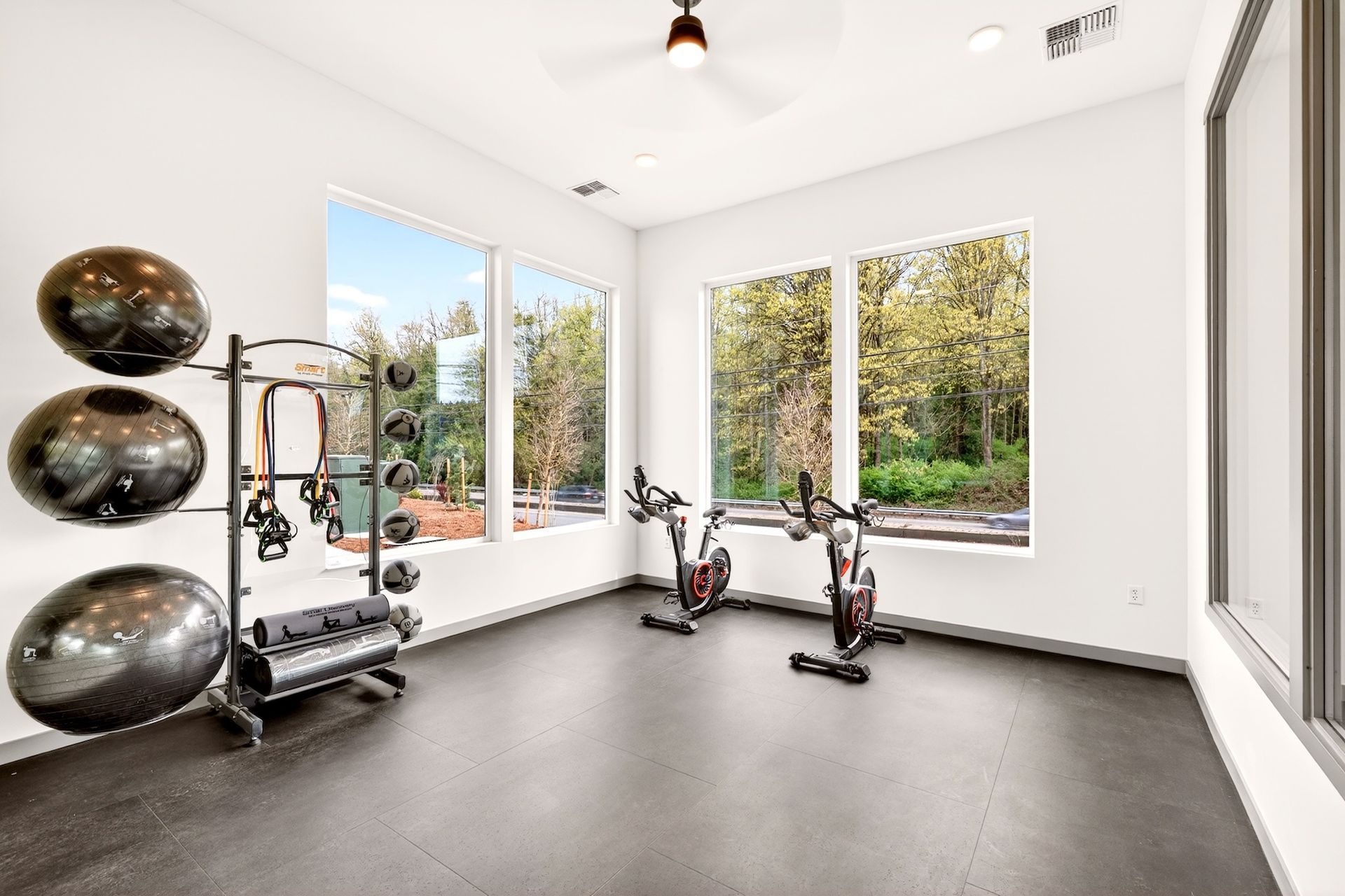 Bright home gym with exercise balls, weight rack, and stationary bikes by large windows