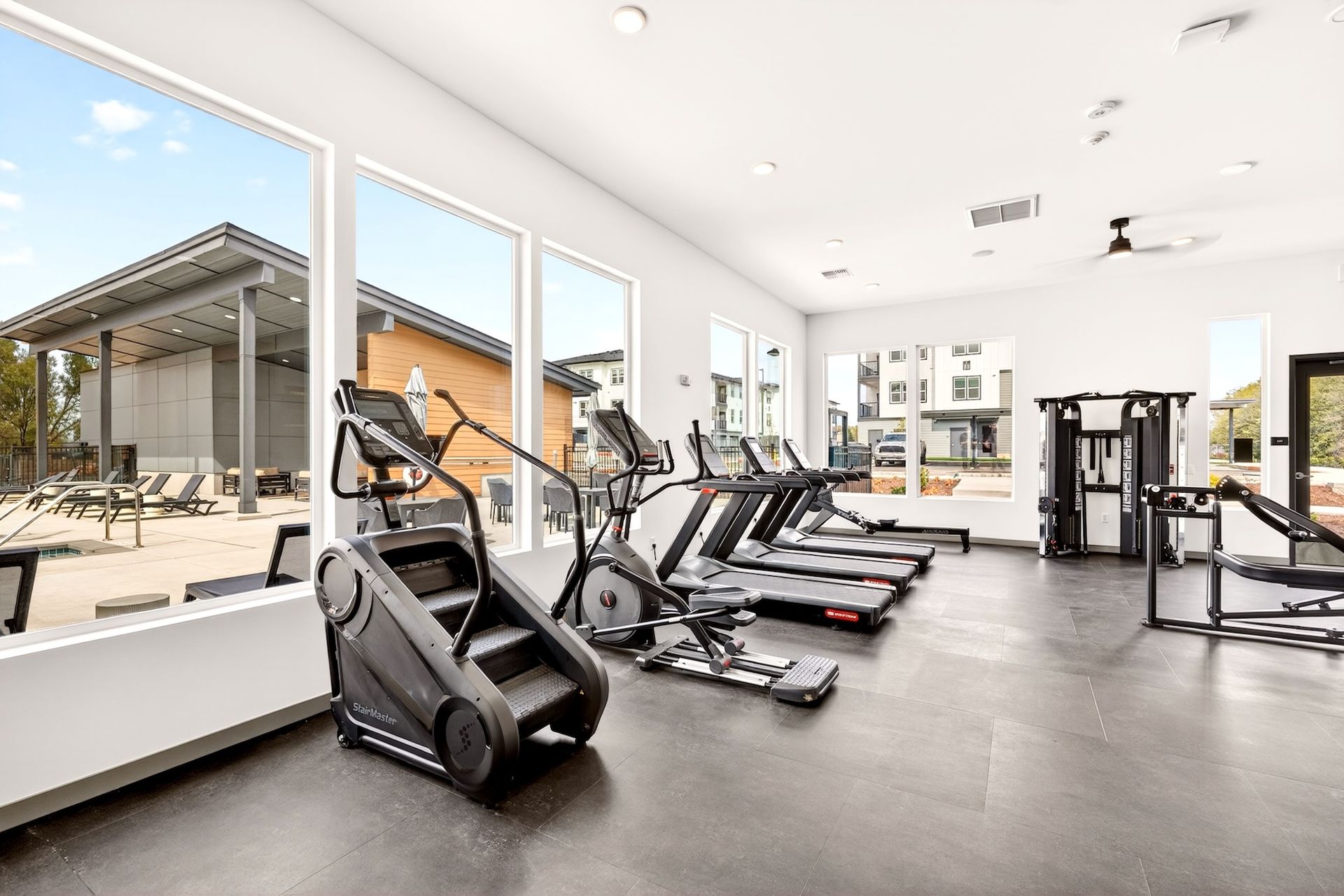 Bright modern gym with treadmills, ellipticals, and large windows overlooking a patio