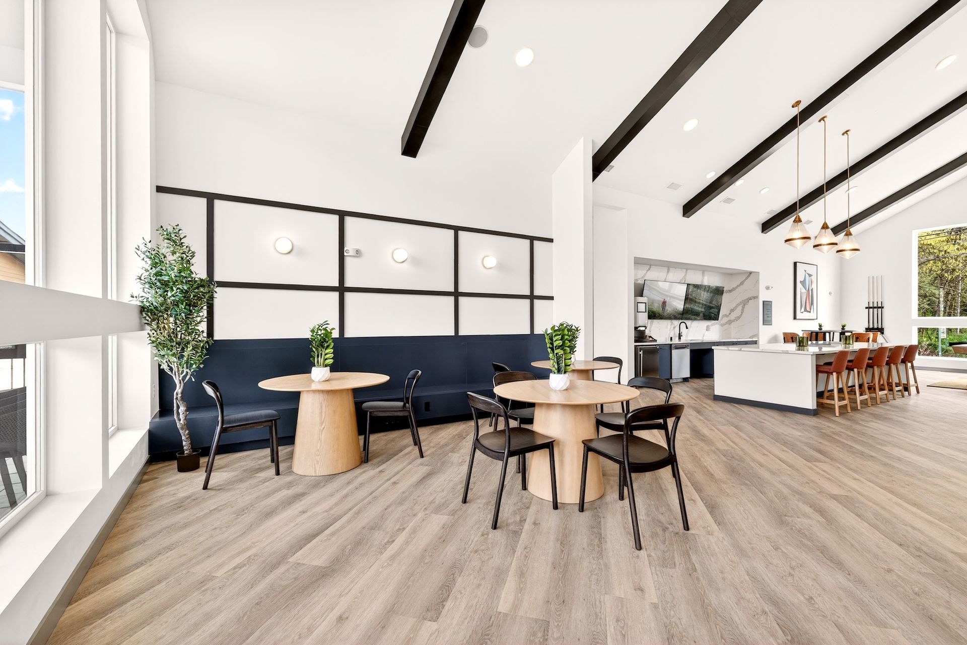 Bright modern cafe interior with round wooden tables, blue banquette seating, and large windows