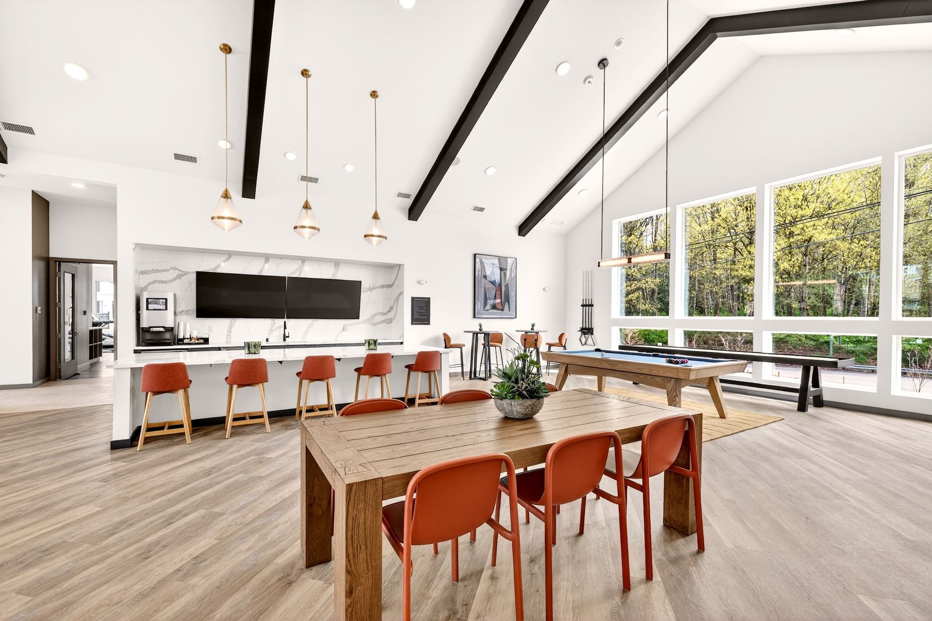 Bright modern kitchen and dining room with orange chairs, long table, and large windows overlooking trees