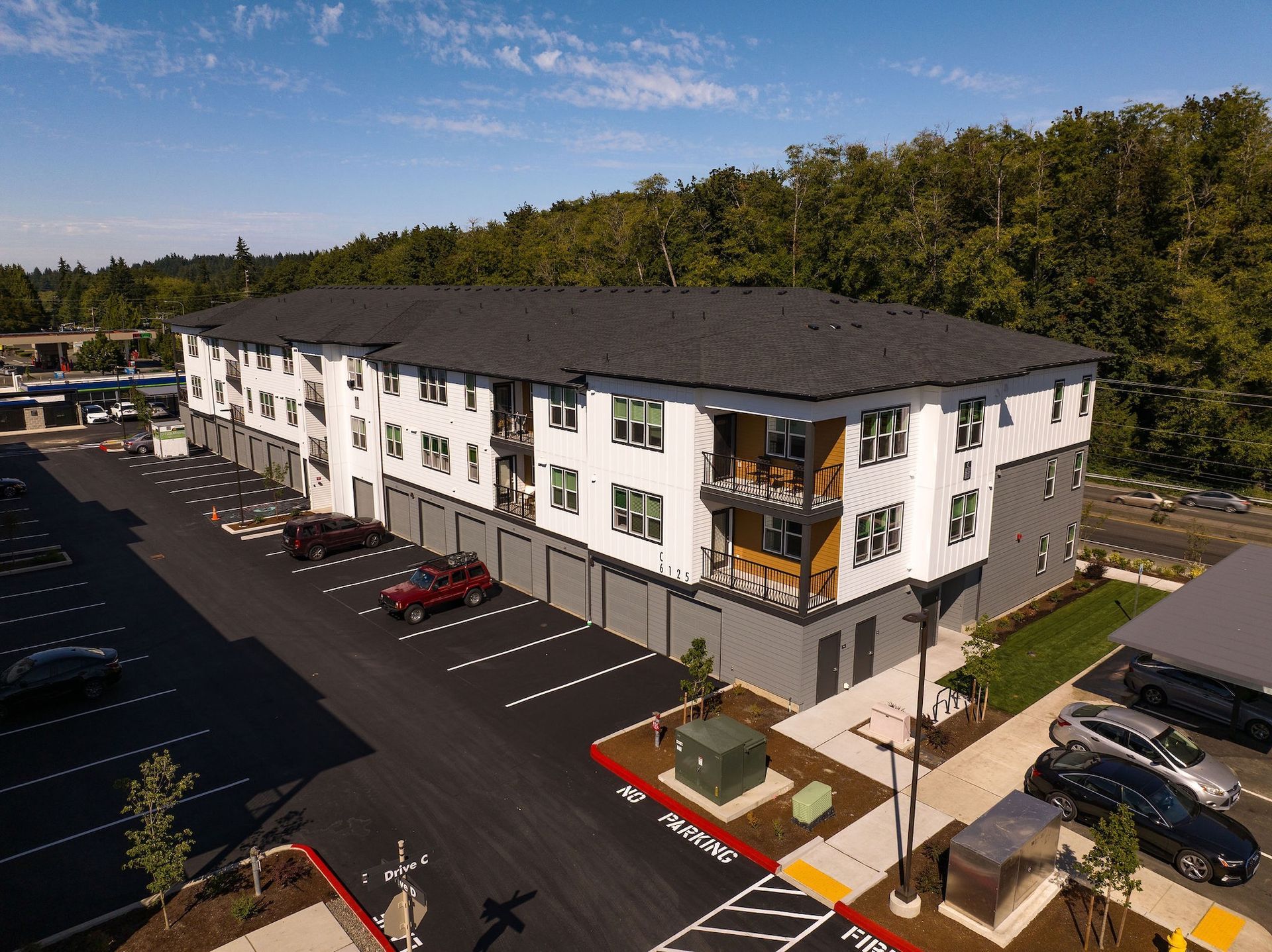 Aerial view of a white apartment building with balconies and a parking lot surrounded by trees