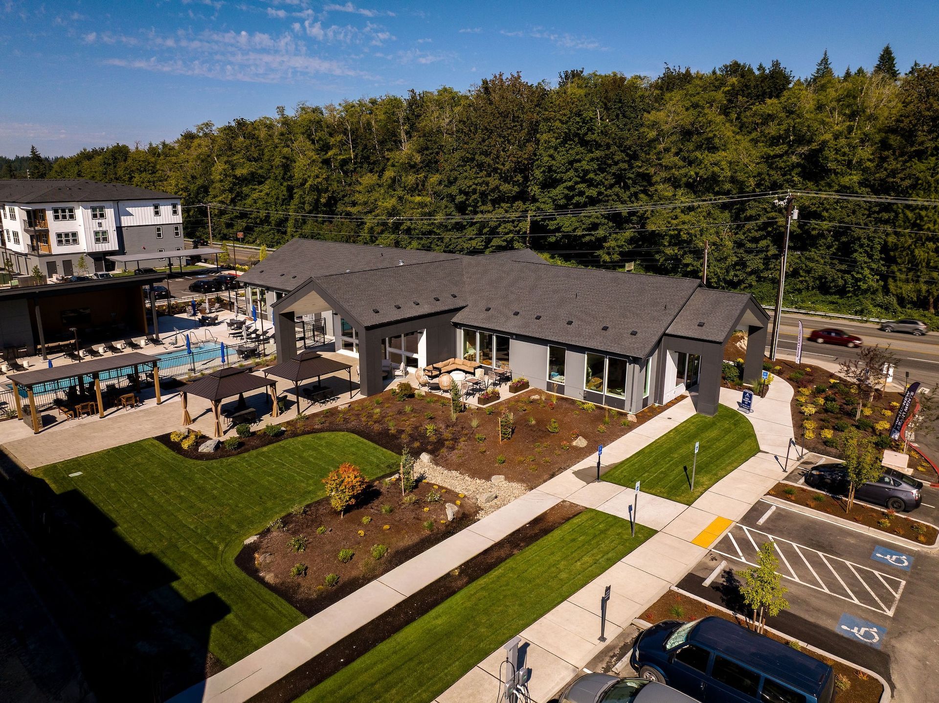 Aerial view of a hotel and pool area beside a wooded hillside and parking lot.